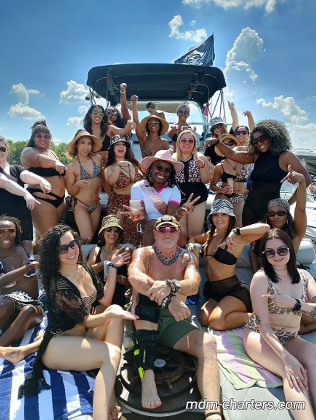 Energetic group of adults in swimsuits posing and cheering on a sunny boat cruise under bright blue skies