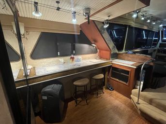 Cozy yacht interior bar area with wooden countertop, two round stools, built-in storage and steps, darkened windows and overhead track lighting.