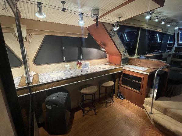 Cozy yacht interior bar area with wooden countertop, two round stools, built-in storage and steps, darkened windows and overhead track lighting.