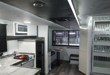 Compact boat-cabin kitchenette with marina view, white cabinets, microwave, glass vessel sink, tiled countertop and mirrored trim.