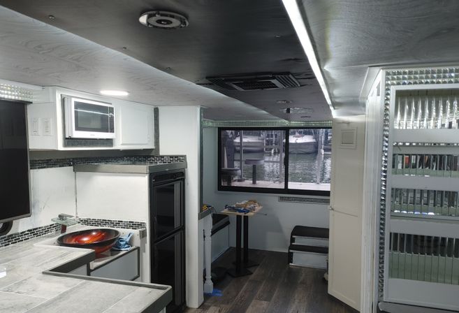 Compact boat-cabin kitchenette with marina view, white cabinets, microwave, glass vessel sink, tiled countertop and mirrored trim.