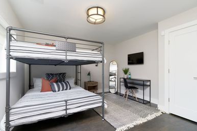 Bright modern bedroom with industrial metal bunk bed, striped bedding, study desk with wall-mounted TV, full-length mirror and woven rug.