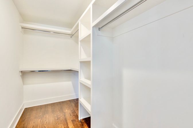 Bright empty walk-in closet with white built-in shelves, chrome hanging rods and warm hardwood floor, ready for organizing