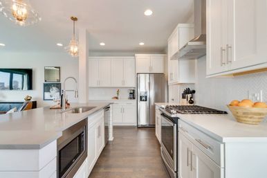 Bright open-concept modern white kitchen with large island, quartz countertops, stainless-steel refrigerator and range, pendant lights, and hardwood floors