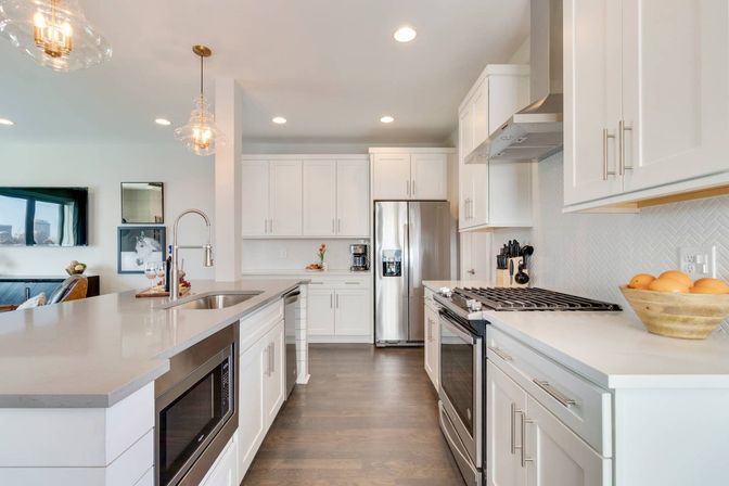 Bright open-concept modern white kitchen with large island, quartz countertops, stainless-steel refrigerator and range, pendant lights, and hardwood floors