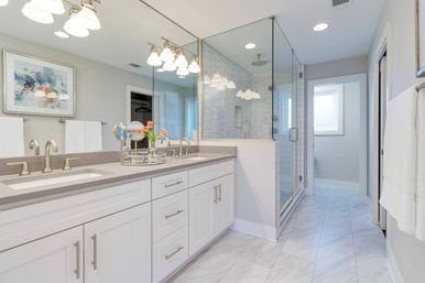 Bright, spa-like modern bathroom with white double-sink vanity, gray quartz countertop, large mirror and pendant lights, glass-enclosed walk-in shower with subway tile, marble-look floor tiles and fresh tulips on the counter.