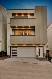 Contemporary three-story townhouse with stacked balconies, warm recessed lights, white two-car garage and driveway at dusk