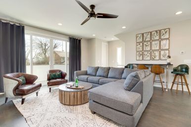 Bright contemporary living room with a gray sectional sofa, two brown leather armchairs, round wooden coffee table, sliding glass doors and ceiling fan