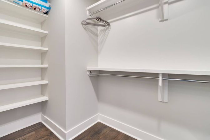 Sleek modern walk-in closet with white built-in shelves, dual chrome hanging rods with a few metal hangers, and dark hardwood floor