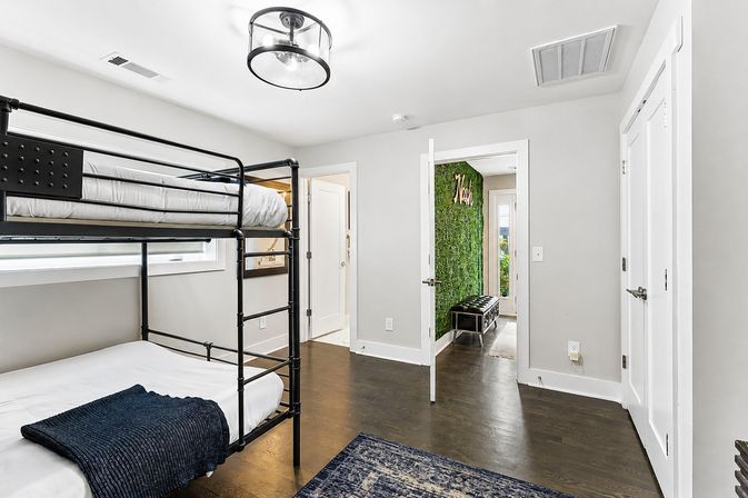Contemporary bunk bedroom with black metal bunk bed, crisp white walls, dark hardwood floors, navy throw and an adjacent room with a green moss accent wall and bench.