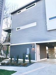 Sleek modern gray two-story townhouse exterior with horizontal lap siding, slim balcony, covered carport, concrete driveway and minimal front landscaping.