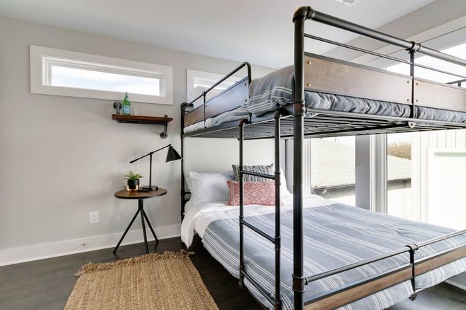 Cozy modern bedroom with industrial black metal bunk bed, striped bedding, large window, round side table, desk lamp and woven rug