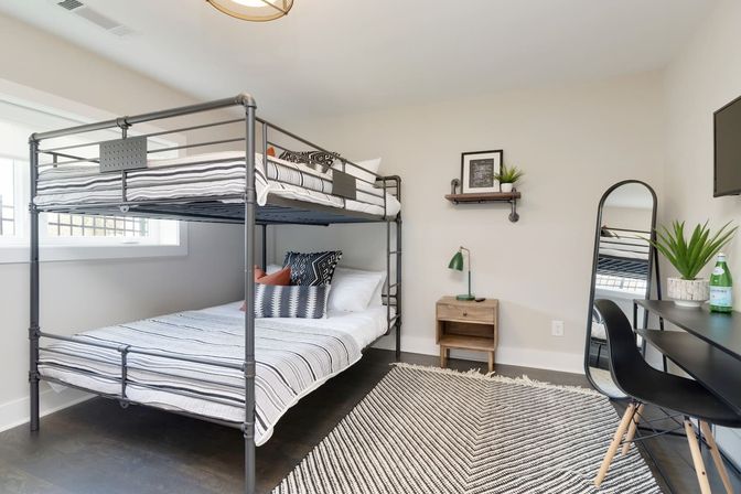Bright modern bedroom with black metal bunk bed, striped bedding, study desk, full-length mirror, wooden nightstand, and geometric rug.