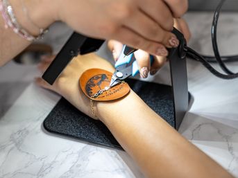 Close-up of jewelry repair: artisan using pliers to adjust a gold bracelet on a wrist over a leather pad under a work lamp on a marble counter