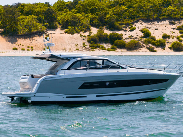 Sleek white luxury motor yacht cruising near a sandy shoreline with dunes and green coastal vegetation on a sunny day