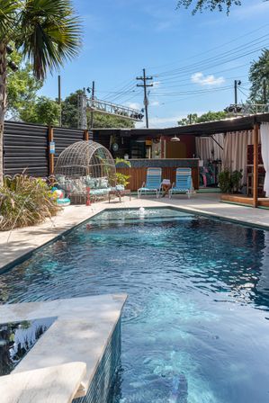 Sunny tropical outdoor pool and poolside lounge with turquoise water, rattan egg-shaped daybed, striped lounge chairs, palm tree and cabana bar — relaxed patio oasis