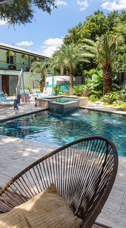 Resort-style outdoor pool courtyard with turquoise water, palm trees, lined lounge chairs and a cabana framed by sheer curtains and wicker seating.