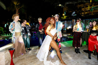 Vibrant poolside night party on an outdoor patio — diverse guests in colorful outfits dancing and laughing around a lit pool, spotlight on a joyful dancer in a flowing white dress