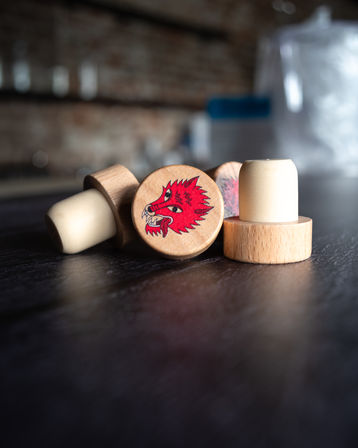 Close-up of wooden pool cue chalk holders on a dark wood tabletop, one stamped with a red wolf head emblem — billiards accessory