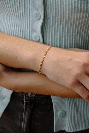 Close-up of a person's wrist wearing a dainty gold floral chain bracelet, styled with a mint ribbed cardigan and dark jeans.