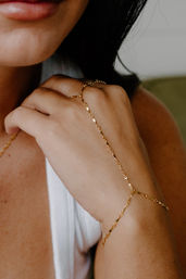 Close-up of woman's hand wearing a delicate gold hand-chain bracelet, minimalist jewelry styled with a white tank top in soft natural light