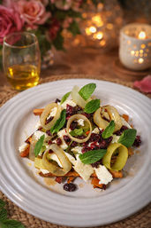 Gourmet roasted carrot and feta salad topped with pickled leek rings, dried cranberries and fresh mint leaves on a white plate in a cozy candlelit table setting