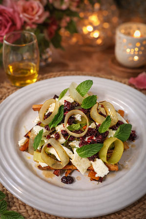Gourmet roasted carrot and feta salad topped with pickled leek rings, dried cranberries and fresh mint leaves on a white plate in a cozy candlelit table setting