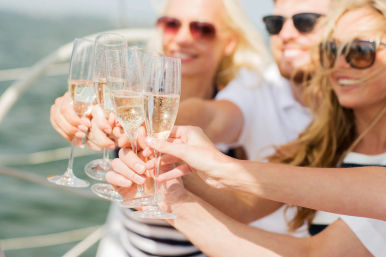 Friends toasting with champagne flutes on a sunny boat cruise over blue ocean water, festive summer celebration