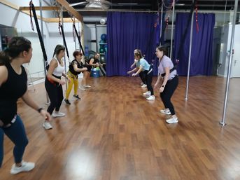 Group of women in harnesses doing a bungee fitness group class in an indoor studio with wood floor and purple curtains.