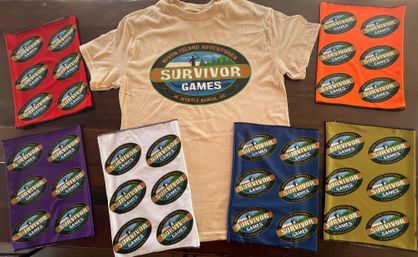 Beige t-shirt with a large oval “Survivor Games” logo (N. Myrtle Beach, SC) at center, surrounded by colorful bandanas/gaiters in red, orange, purple, white, blue and olive each printed with repeated smaller “Survivor Games” logos, laid out on a dark table.