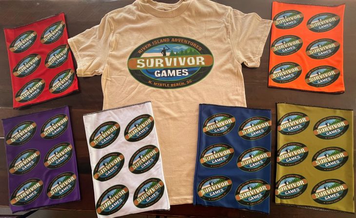 Beige t-shirt with a large oval “Survivor Games” logo (N. Myrtle Beach, SC) at center, surrounded by colorful bandanas/gaiters in red, orange, purple, white, blue and olive each printed with repeated smaller “Survivor Games” logos, laid out on a dark table.