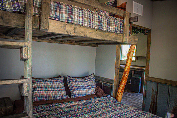 Cozy rustic bedroom with reclaimed wood bunk beds, plaid bedding, and a knotty wood ladder.