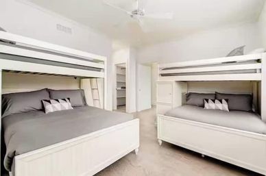 Bright, airy bedroom with two white twin-over-full bunk beds, gray bedding and geometric accent pillows, ceiling fan and open closet — modern family-friendly sleeping area.