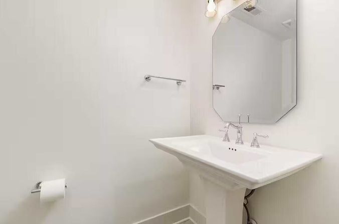 Bright minimalist residential powder room — white pedestal sink, octagonal mirror, chrome faucet and towel bar with toilet paper holder.