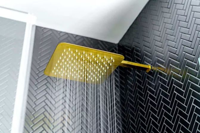 Wall-mounted gold square rain showerhead spraying water against matte black herringbone tile in a modern bathroom