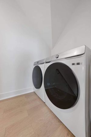Minimal modern laundry room with matching white front-load washer and dryer side-by-side on light hardwood floors against plain white walls