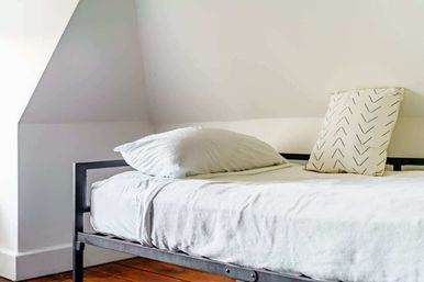 Cozy minimalist attic bedroom with white linens, arrow-pattern throw pillow on a black metal bed frame and warm hardwood floor
