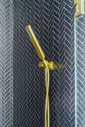 Gold handheld shower and flexible hose mounted on dark herringbone tile wall in a modern bathroom shower