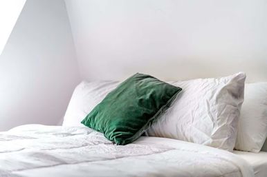 Minimalist bright bedroom with a green velvet accent pillow resting on crisp white pillows and a white duvet