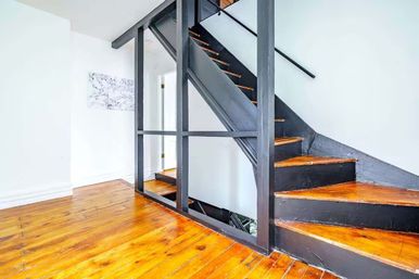 Bright, modern loft-style interior featuring a black open-frame staircase and glossy honey-toned hardwood floors against white walls