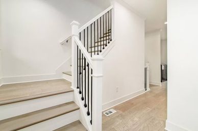 Bright modern home entry with white painted staircase, light wood treads, black metal balusters and matching light hardwood floors in a minimalist hallway.