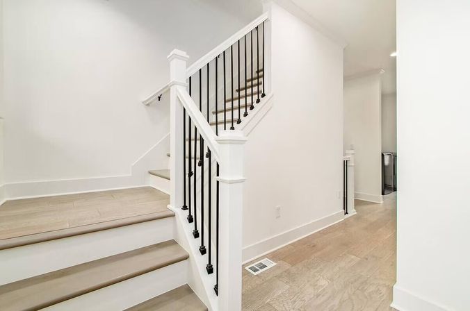 Bright modern home entry with white painted staircase, light wood treads, black metal balusters and matching light hardwood floors in a minimalist hallway.