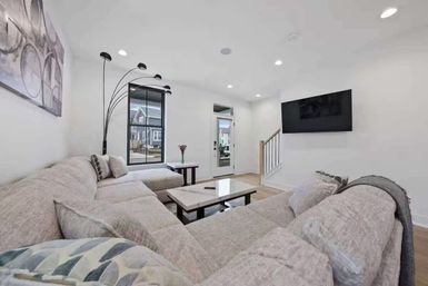 Bright modern suburban living room with large beige sectional, wall-mounted TV, marble coffee table, arched floor lamp, recessed lighting and hardwood floors