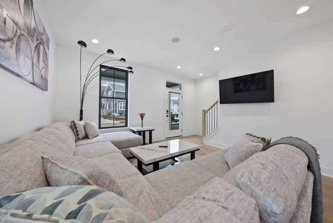 Bright modern suburban living room with large beige sectional, wall-mounted TV, marble coffee table, arched floor lamp, recessed lighting and hardwood floors