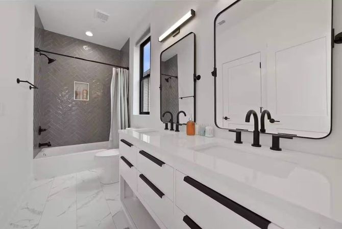 Sleek contemporary white bathroom with double vanity, matte black faucets and hardware, large rounded-rectangle mirrors, marble-look floor tile, and a gray herringbone-tiled bathtub/shower with curtain and window.