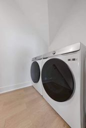 Sleek matching white front-load washer and dryer with large black circular doors on light wood floors in a bright minimalist laundry room