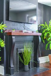 Modern black fireplace with wooden mantel and herringbone tile surround, wall-mounted flat-screen TV above and potted green indoor plants adding a pop of color on hardwood floors in a contemporary living room.
