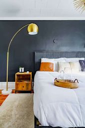 Modern bedroom interior with matte black accent wall, gold arched floor lamp, wooden nightstand, white duvet bed with leather accent pillow and wooden tray — cozy minimalist bedroom decor.