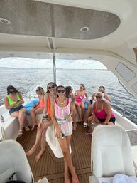 Group of women in colorful swimsuits and sunglasses enjoying a daytime boat party on a yacht deck with calm ocean and distant coastline