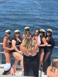 Bachelorette party on a boat: women in bikinis and captain hats, one wearing a veil, posing for a group photo on a sunny ocean cruise